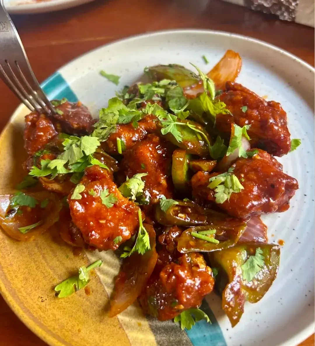 A saucy chilli dish with peppers and coriander in a shallow bowl.