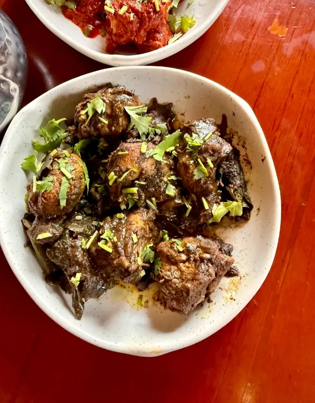 A bowl of dark, dry-fried meat with green chilli and coriander.