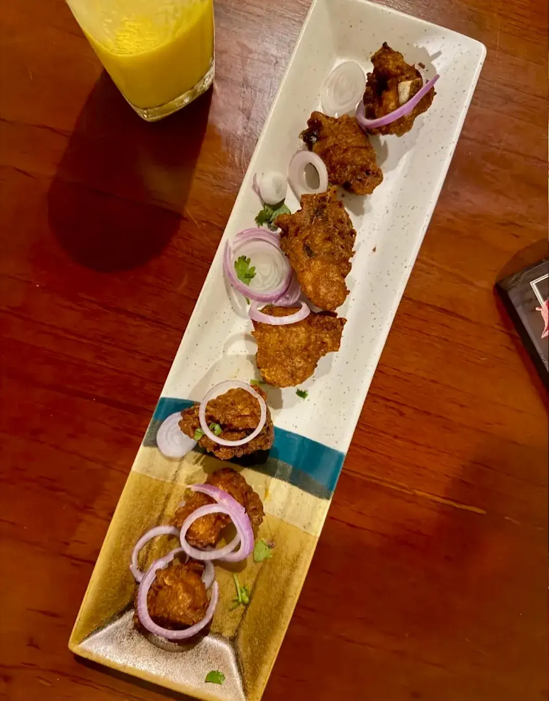Skewered kebabs on a long plate with sliced onion and a dipping bowl.