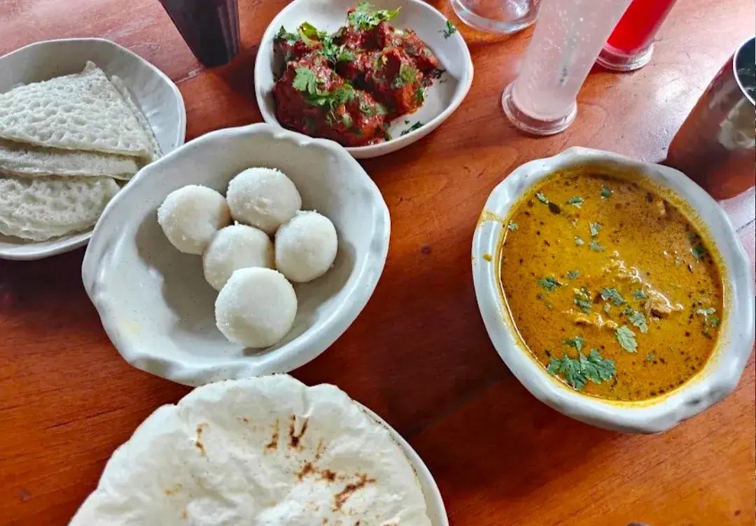Steamed rice dumplings, flatbreads and a bowl of curry set out on a table.