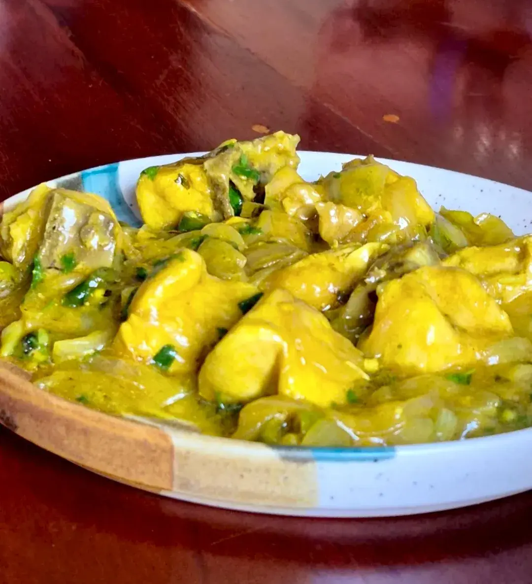 A pale yellow curry with potato and green chilli in a wide ceramic bowl.