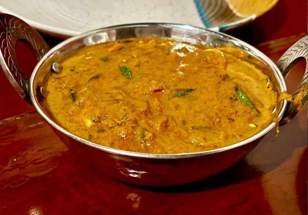 A copper-rimmed bowl of thick yellow curry.