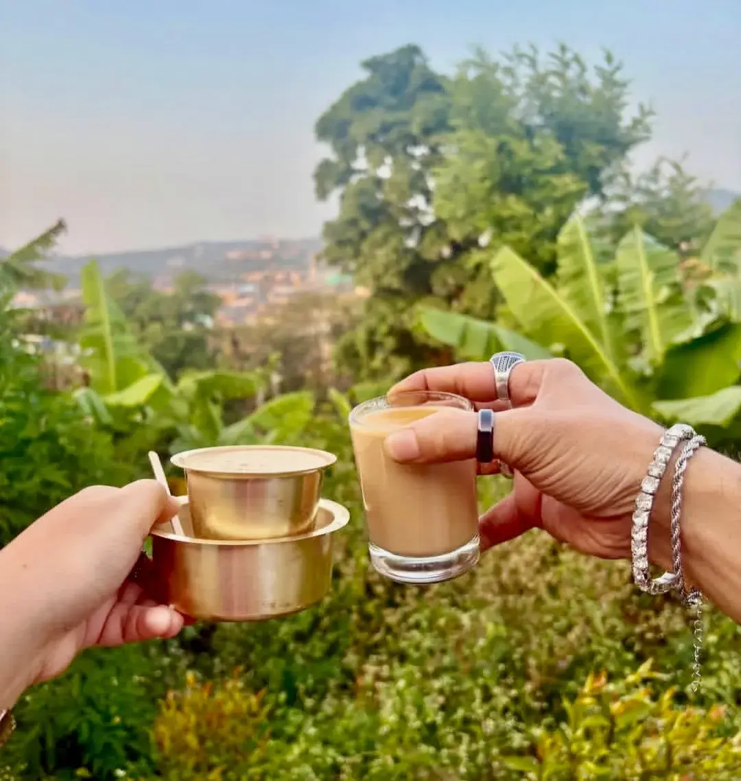 Two brass tumblers of filter coffee held up against the green hills.
