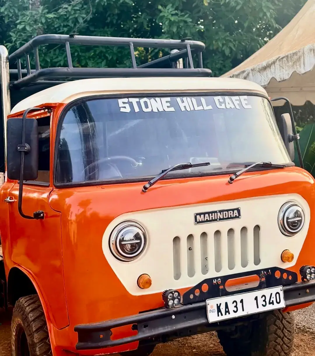An orange Mahindra jeep parked on the property, “Stone Hill Cafe” lettered across its windscreen.